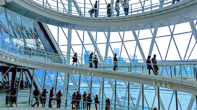 Wide angle color image depicting ultra modern contemporary interior architecture in City Hall (a public building in London that is open to the public) in London, UK. Crowds of people in silhouette and unrecognizable are walking down the modern spiral staircase. In the background we can see some of the skyscrapers that dominate the skyline of London. Lots of room for copy space.